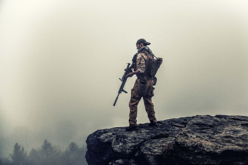 Field operator standing on a rocky outcrop overlooking remote, fog-covered terrain
